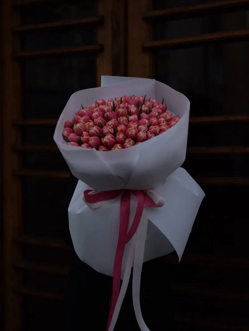 Duży bukiet różowych tulipanów w białym papierze, przewiązany wstążką